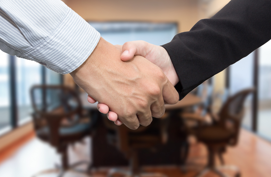 Close up of businessmen shaking hands in meeting room.