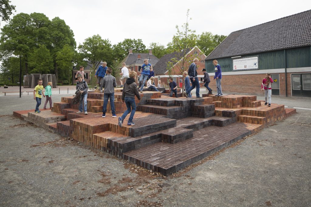 ‘Back to the Roots’ creates an attractive new meeting place at the Heritage Square located in the heart of the village of Slochteren. Centred around a tree, the terraced landscape becomes a multi-sided podium, tribune, playground and exhibition space all in one. The 30,000 multi-coloured, textured bricks are laid in a way that forms an earthy camouflage-like gradient stepping up towards the tree, and then back down creating seating around its trunk.
