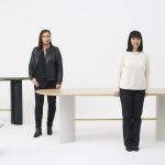 Two women dressed in white and black standing around designer tables. Miriam Fanning.
