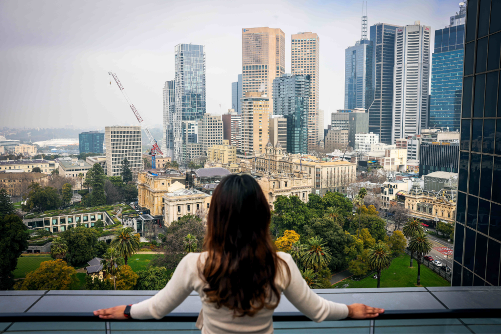 Lanson Place. On a high balcony we see the back of a woman with long brown hair looking down over the city.