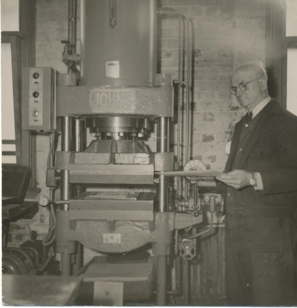 Lanson Place Salvation Army printing press archival image, with an older balding and bespectacled man standing next to the press inspecting the work