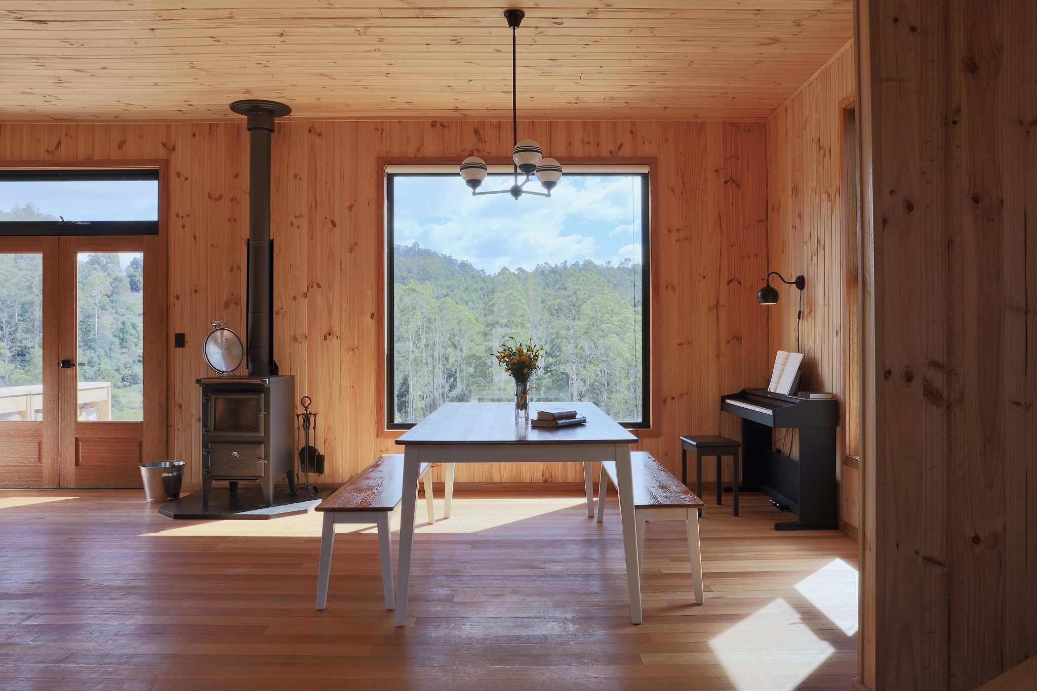 Jiri Lev, interior of wooden house with simple furnishings, including a stove with a chimney through the ceiling and an electric keyboard
