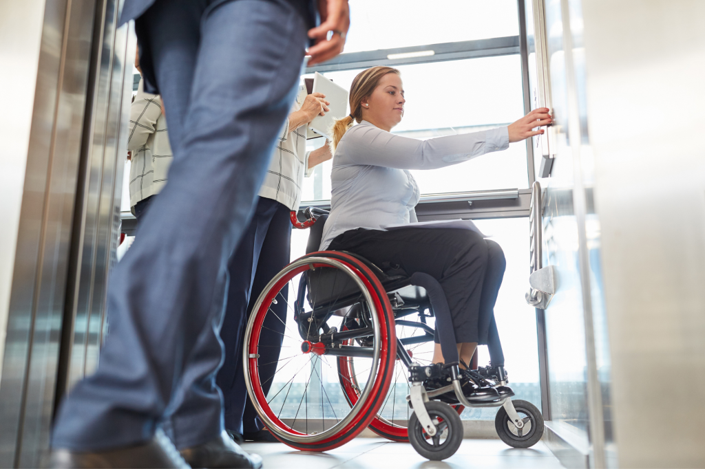 Three people are in a life. One is a wheelchair user and she is pushing the button.